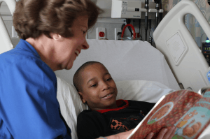 Featured Image for Volunteer reading to young boy in hospital bed